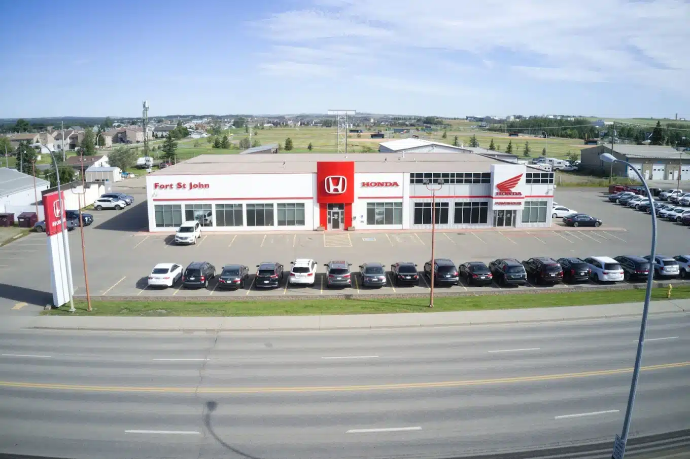Aerial view of a Honda dealership in Fort St John, featuring parked cars and surrounding scenery.