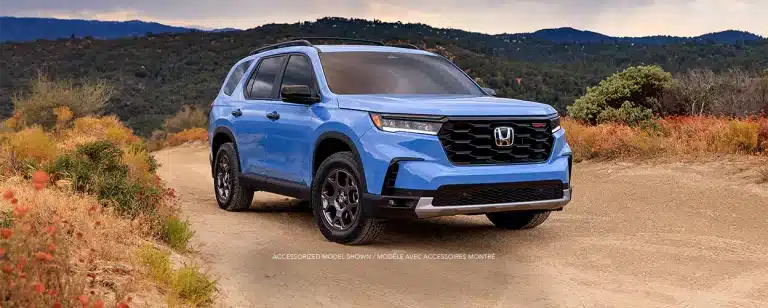 Blue Honda SUV on a dirt road in a scenic mountainous landscape.