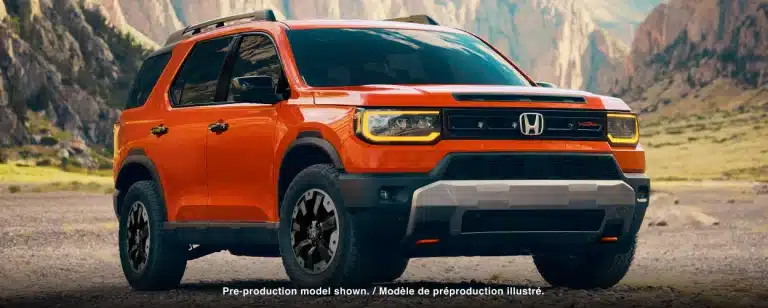 Orange Honda SUV on rocky terrain with mountains in the background, showcasing bold design.