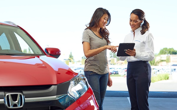 Customer discussing options with a sales representative near a red Honda car at a dealership.