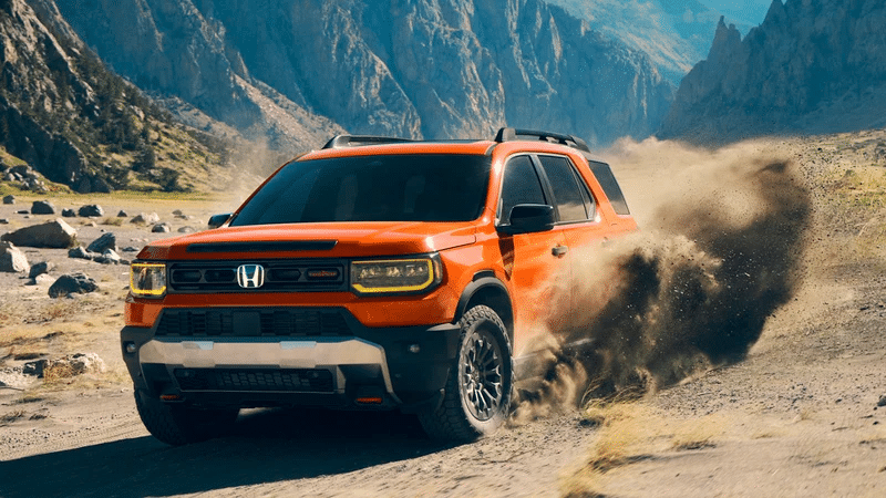 Orange SUV driving off-road, kicking up dust, with rugged mountain scenery in the background.