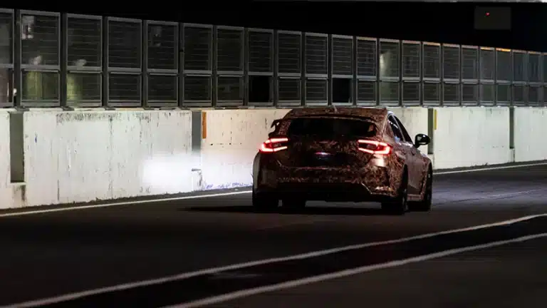 Camouflaged car with headlights on, driving through a dimly lit tunnel.