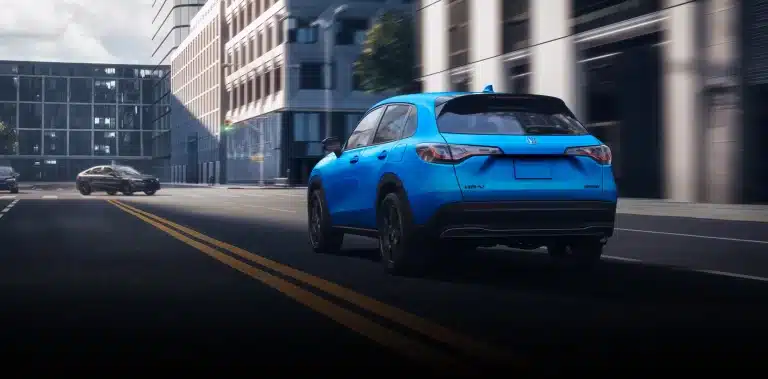 A blue SUV driving down a city street, flanked by modern buildings.