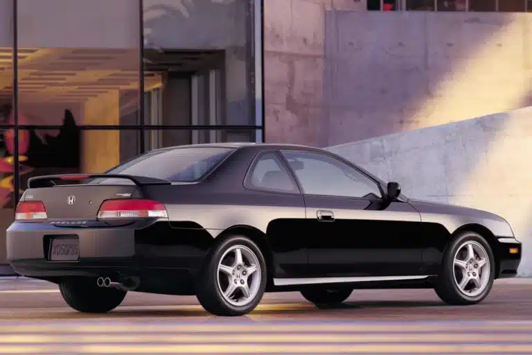 Black Honda Prelude sports car parked beside modern building, showcasing sleek design and alloy wheels.