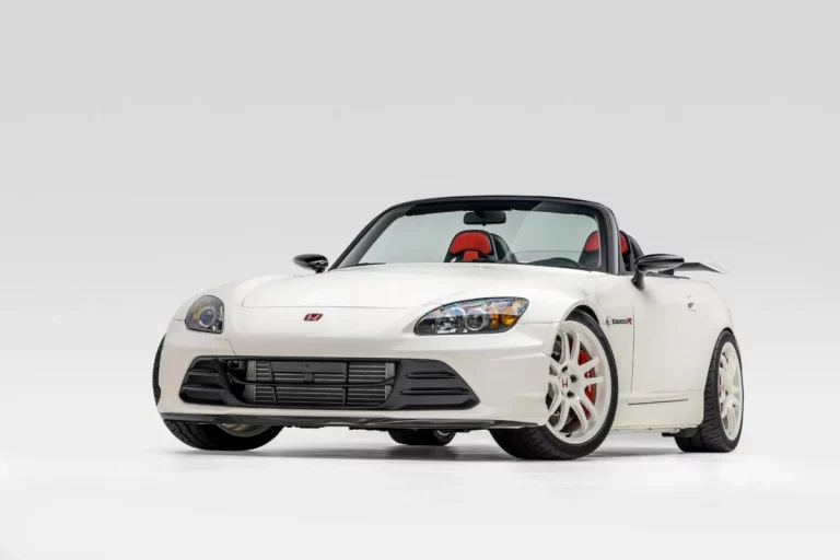 White convertible sports car with red accents and black soft top against a plain background.