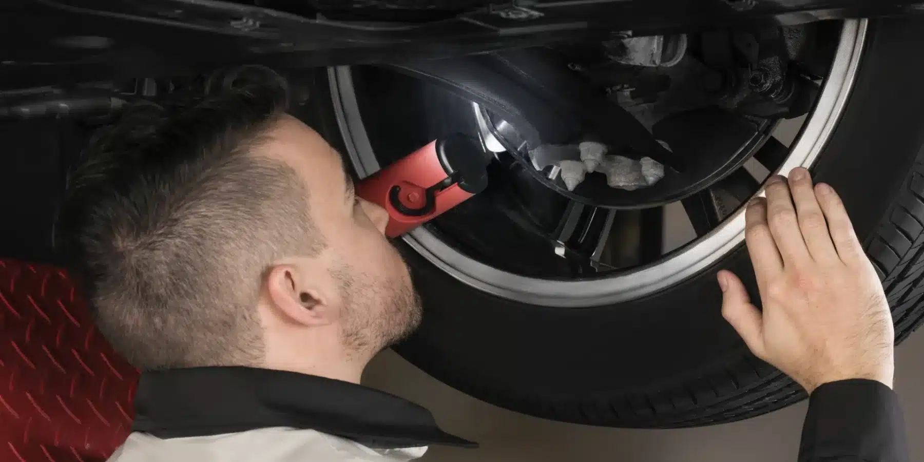 Mechanic inspecting car wheel with a flashlight, focusing on the tire and rim details.