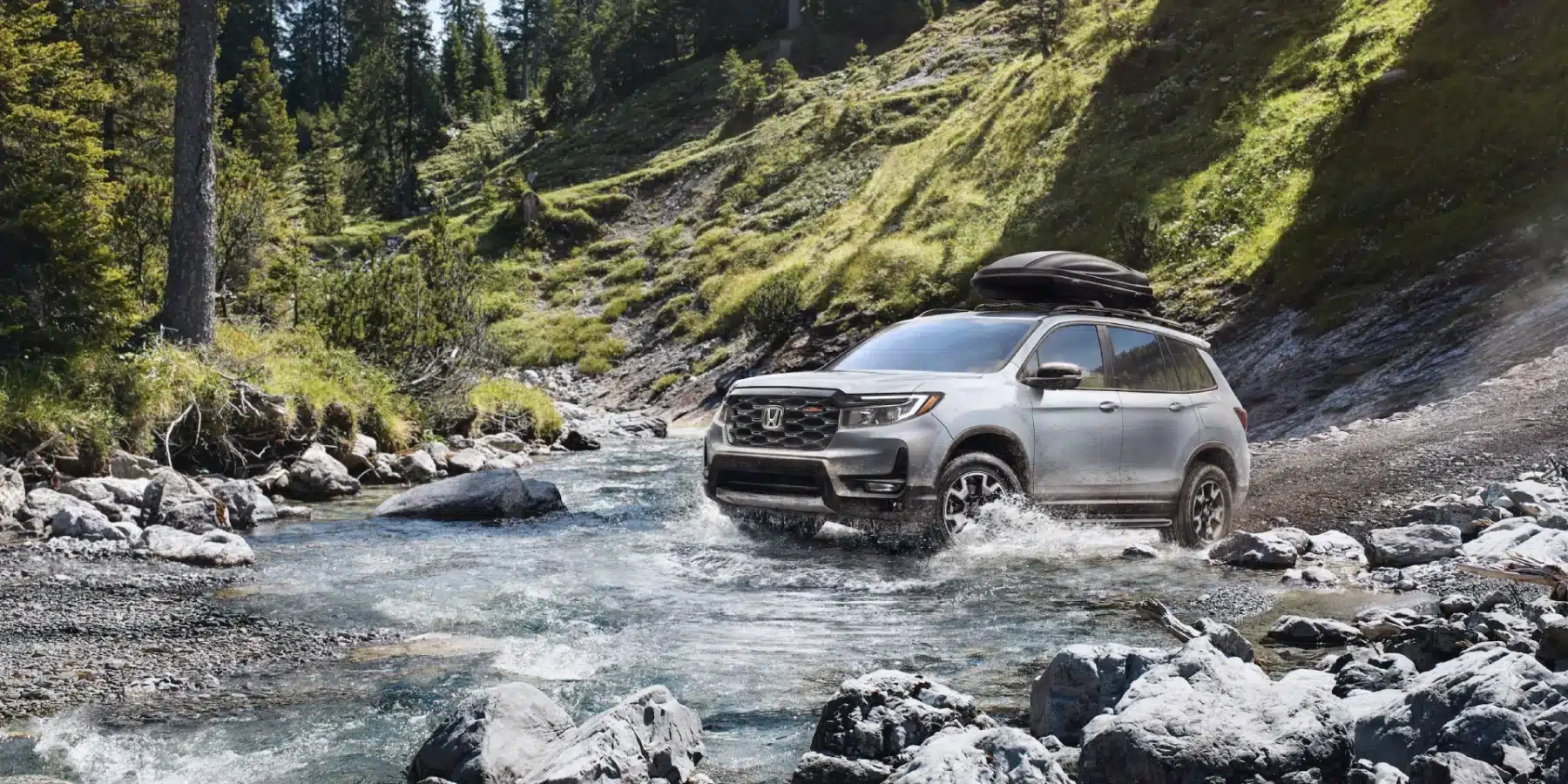SUV driving through a rocky stream in a lush forested mountain landscape, showcasing off-road capabilities.